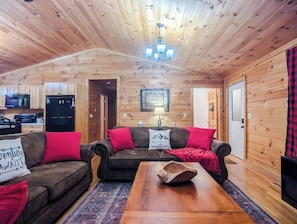 Ein gemütliches Blockhaus-Interieur mit Holzbalkendecke, einer Sofagarnitur, einem Couchtisch und einer Küchenzeile.