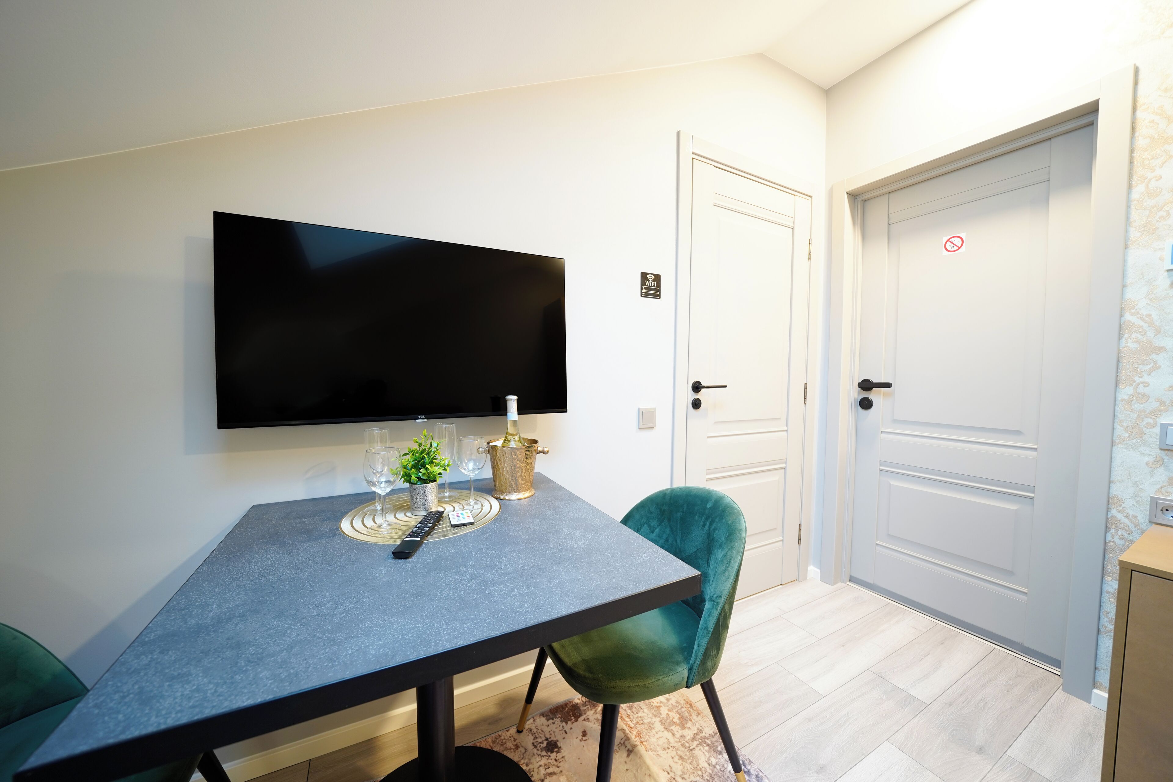 A modern room with a flat-screen TV mounted on the wall, a dining table with chairs, a small plant, and a wine bottle.