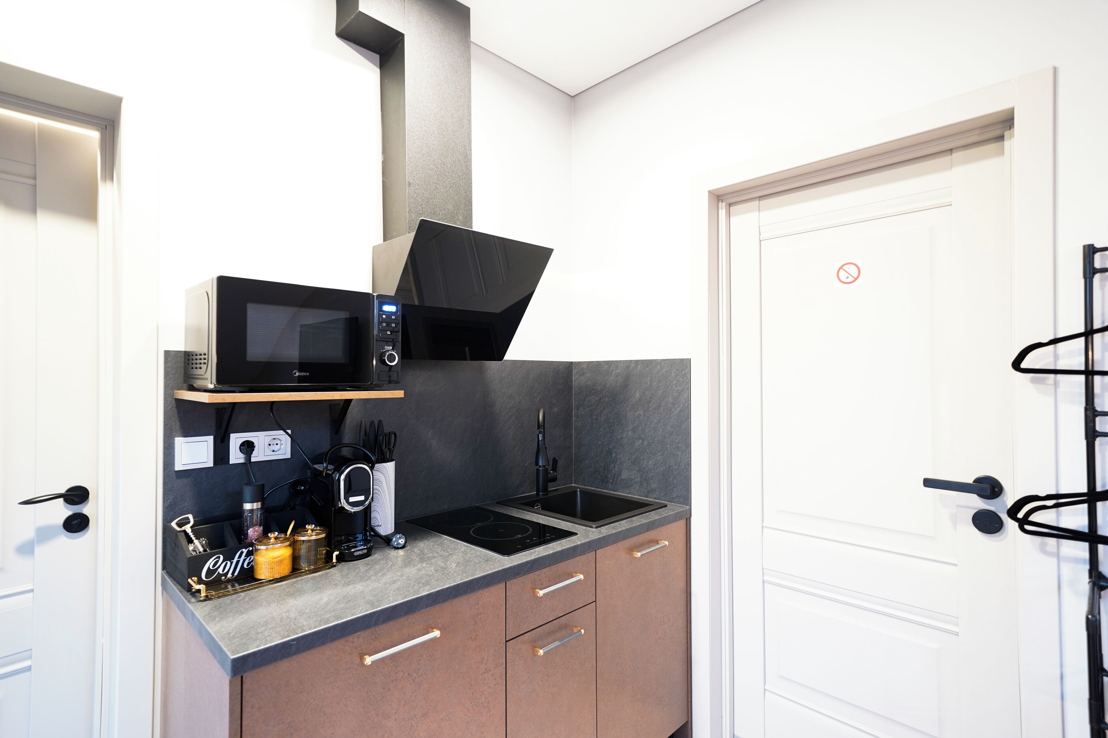 A compact kitchen with a microwave, coffee machine, and a sink. There are cabinets with handles and a small countertop area.
