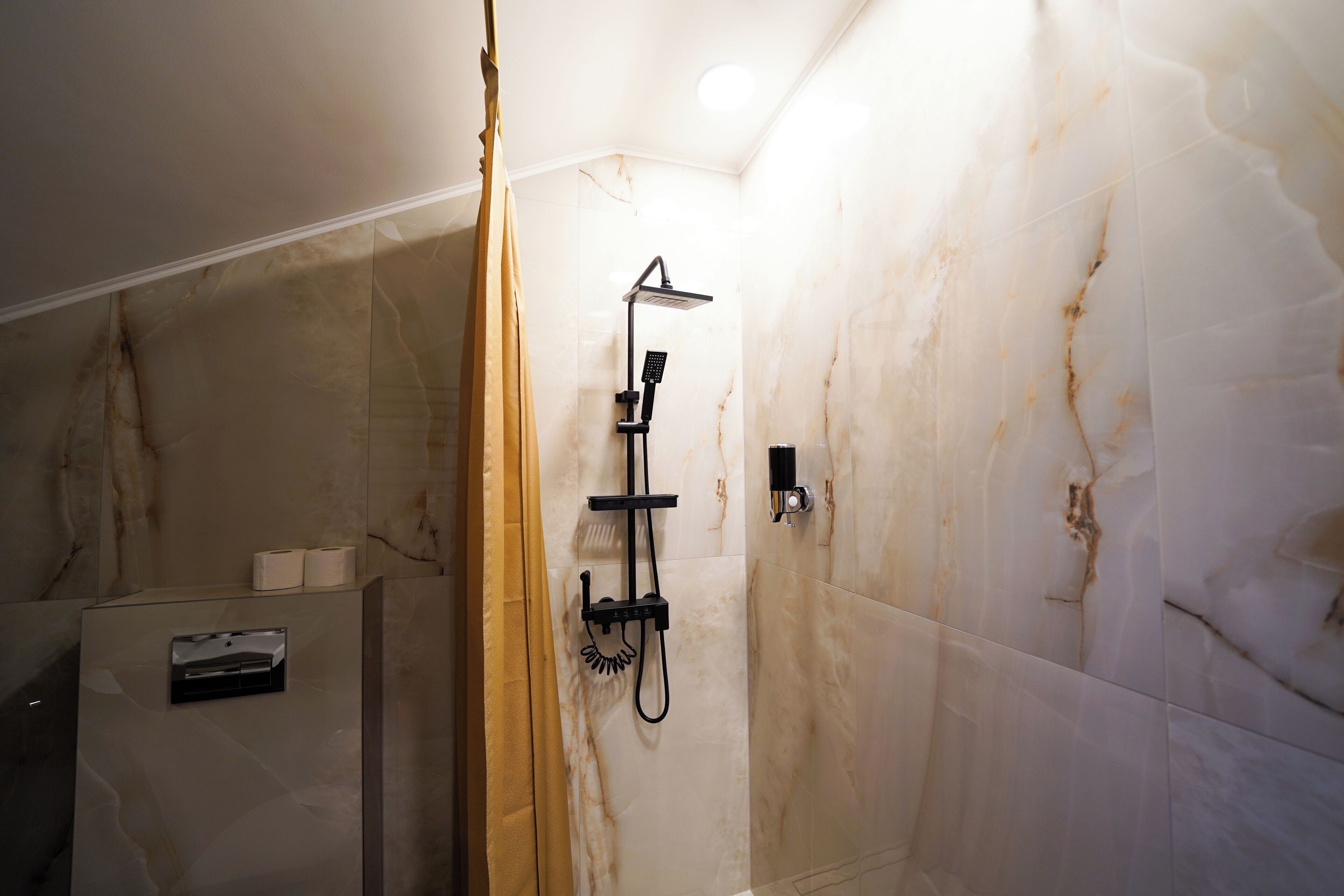 A bathroom with a shower, marble walls, and a toilet paper dispenser.