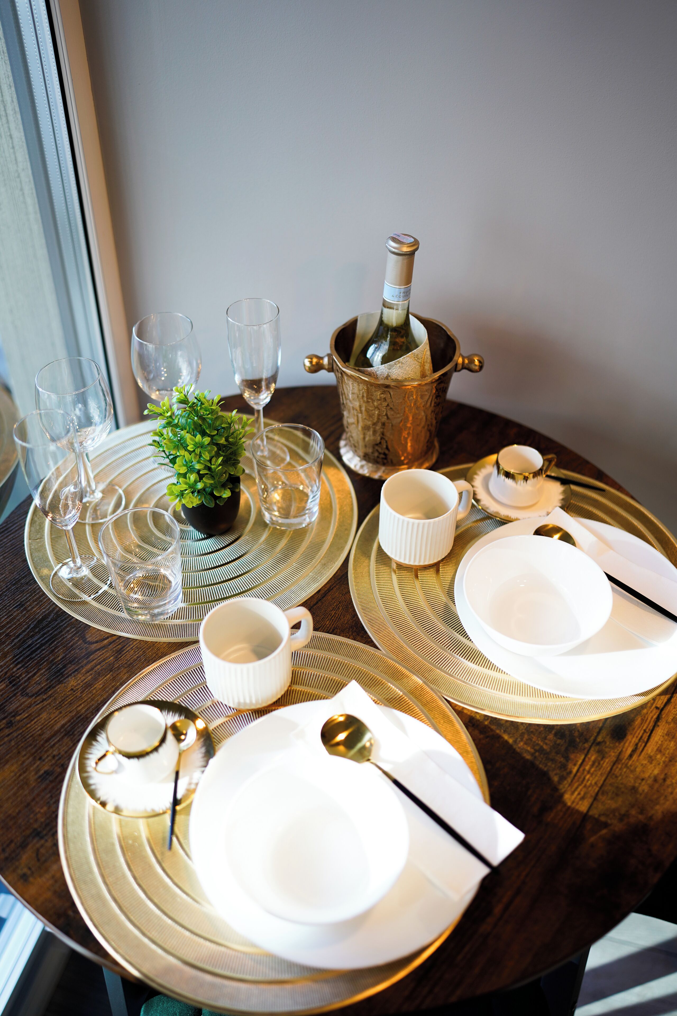 A table set with white plates, glasses, and a small plant.