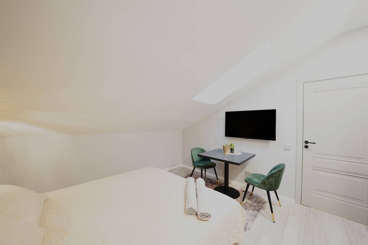 A bedroom with a bed, two chairs, a small table, a flat-screen TV, and a door.