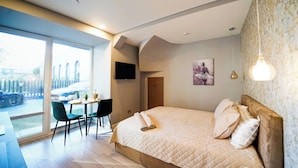 A modern bedroom with a large bed, a dining area with chairs, a table, and a view of the outside. - Svaja ApartHotel & Spa (Šiauliai)