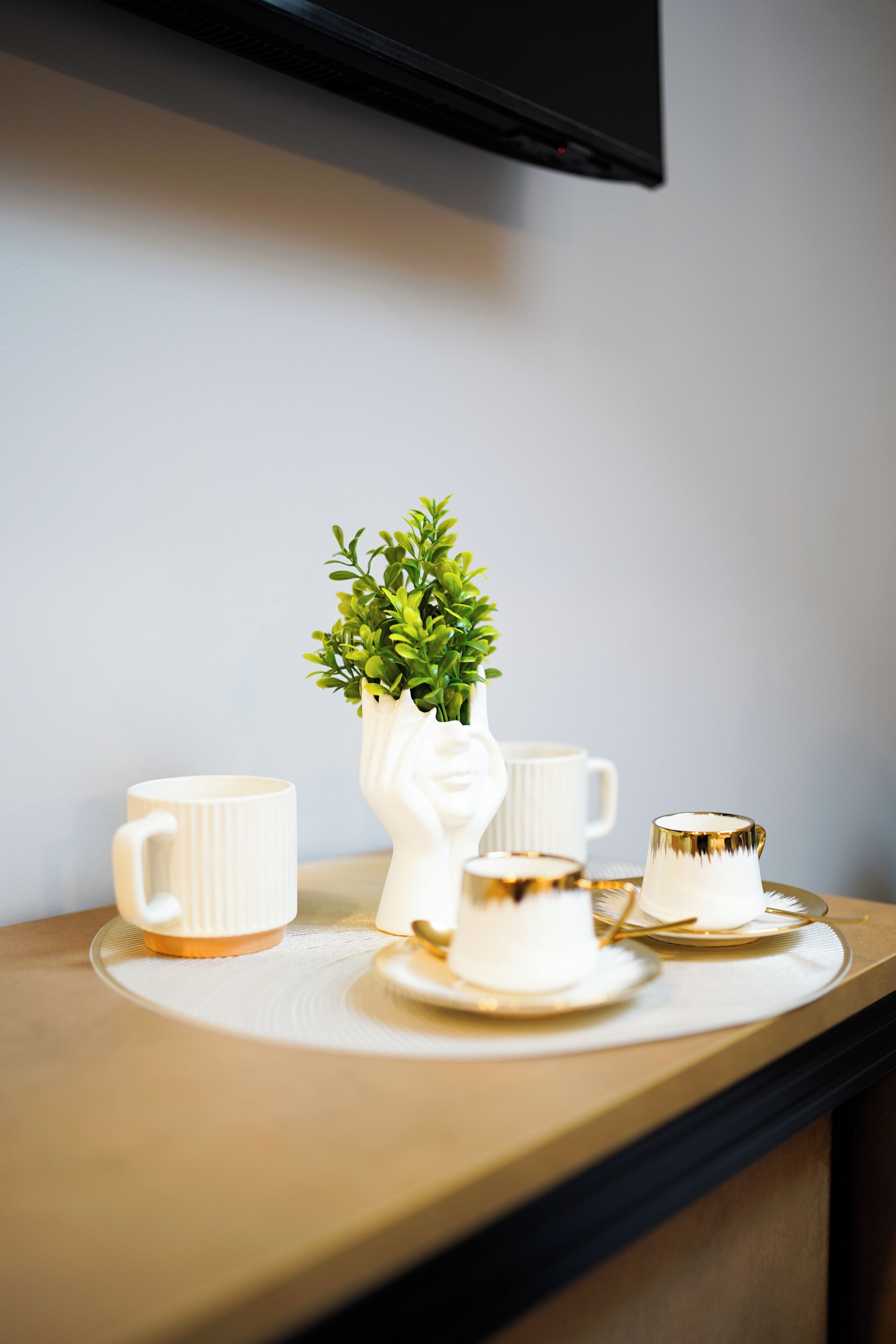 A table with a white ceramic pitcher, two white cups, and a small potted plant.