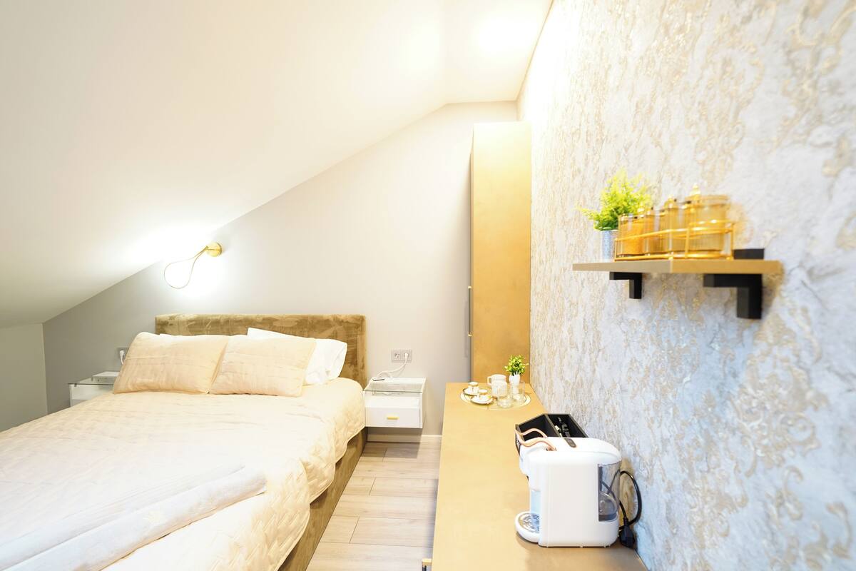 A modern bedroom with a bed, bedside table, and a wall-mounted shelf with a plant and candles.
