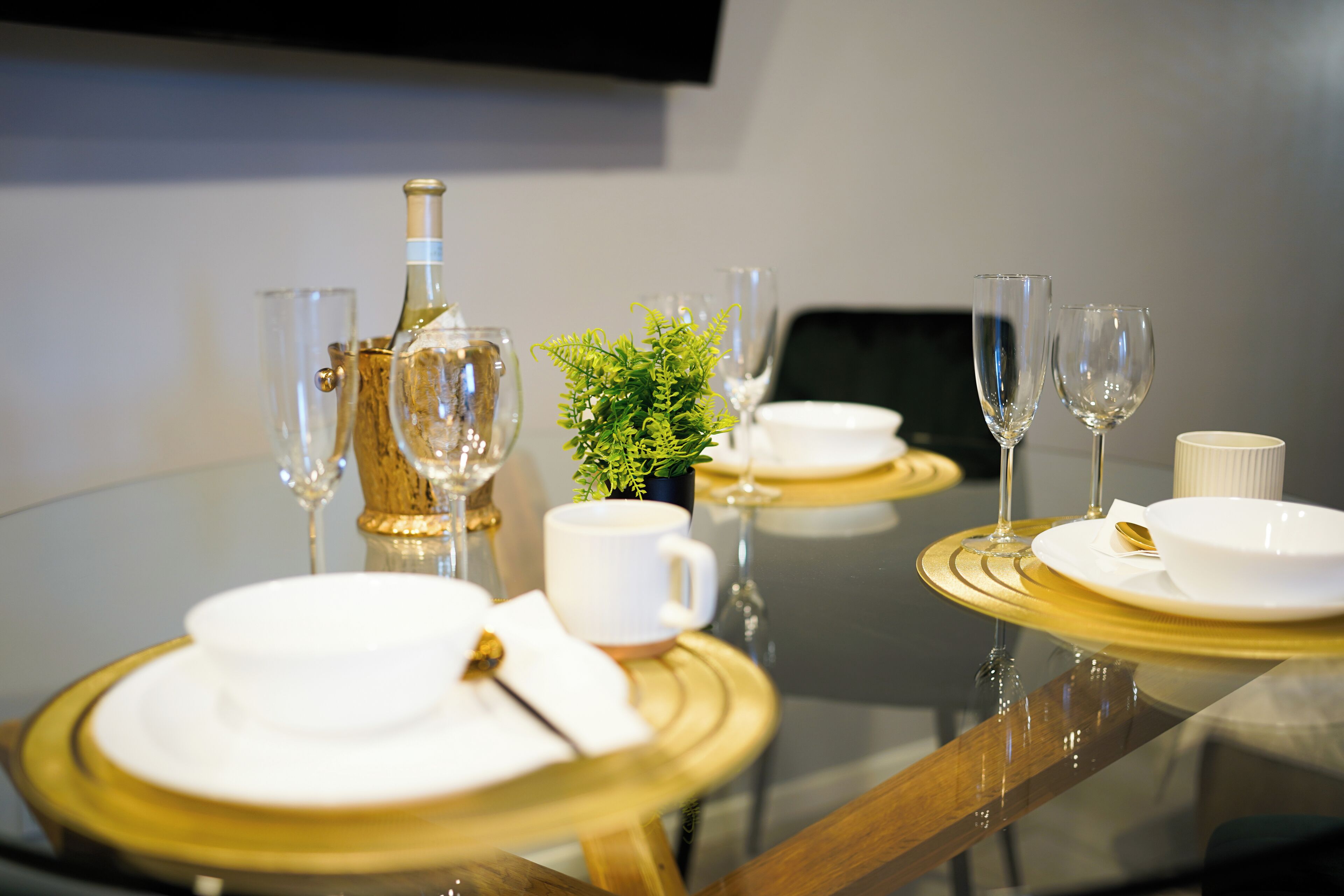 A dining table set with white plates, gold-rimmed bowls, and clear wine glasses.