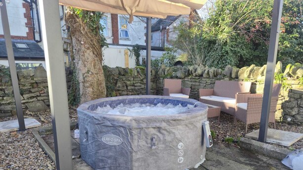 Una vasca idromassaggio sotto una pergola in un giardino con pareti in pietra e mobili da esterno.