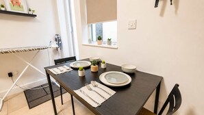 Un'area pranzo con un tavolo in legno scuro apparecchiato per due persone, piatti bianchi, posate e una piccola pianta in vaso.