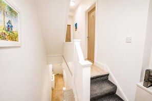 A narrow hallway with a wooden door at the end, a white wall, and a small framed picture on the left. - Cardiff Studio on Claude Road | Fast WiFi & Double Bed (Cardiff)