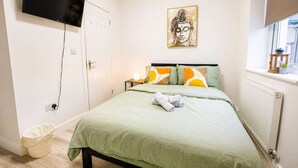 Una camera da letto con un letto, una TV a parete, un quadro, un termosifone e una finestra con vista.