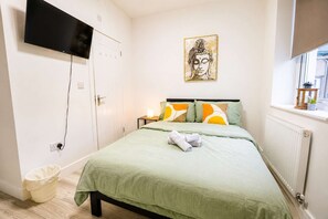 Ein Schlafzimmer mit einem Bett, einem an der Wand montierten Fernseher, einem Gemälde, einer Heizung und einem Fenster mit Blick.