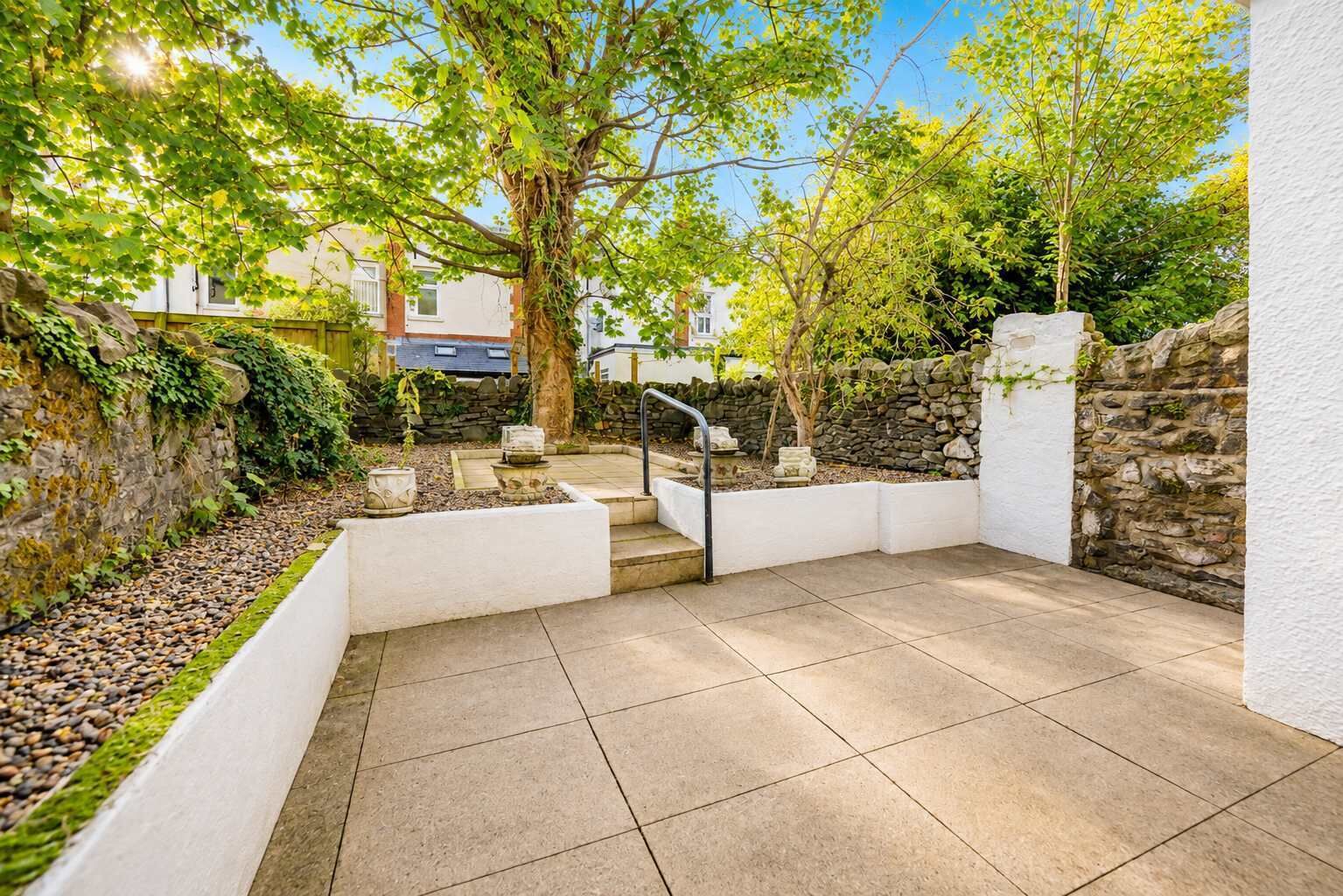 Eine Terrasse mit Steinmauer, weißem Geländer und gefliestem Boden.