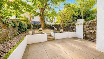 Eine Terrasse mit Steinmauer, weißem Geländer und gefliestem Boden.