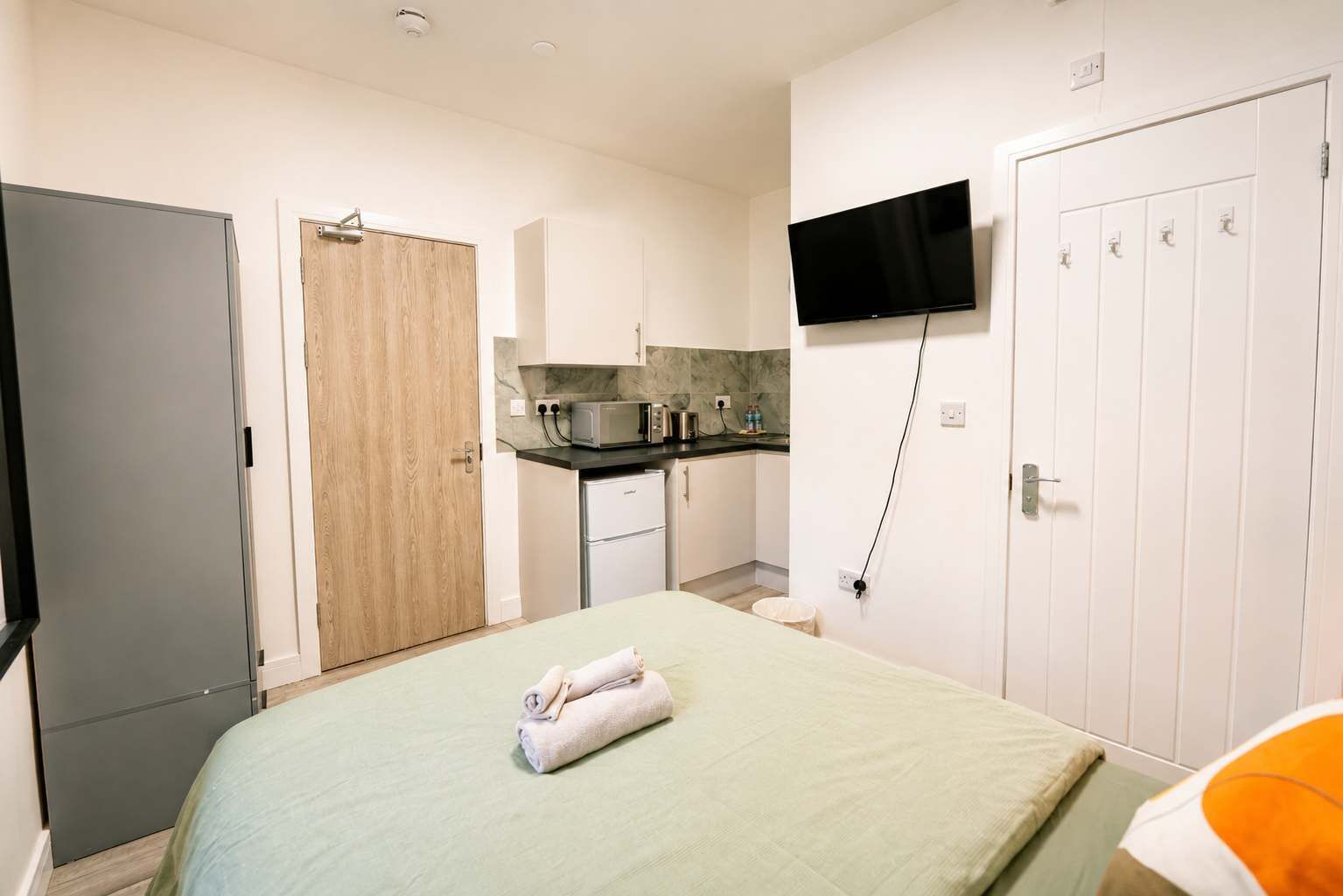 Ein Schlafzimmer mit einem Bett, einem an der Wand montierten Fernseher, einer Küchenzeile und einem Kleiderschrank.