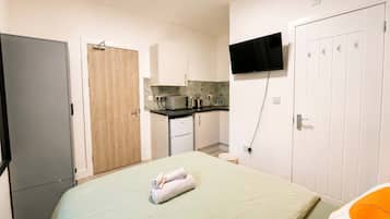 Ein Schlafzimmer mit einem Bett, einem an der Wand montierten Fernseher, einer Küchenzeile und einem Kleiderschrank.
