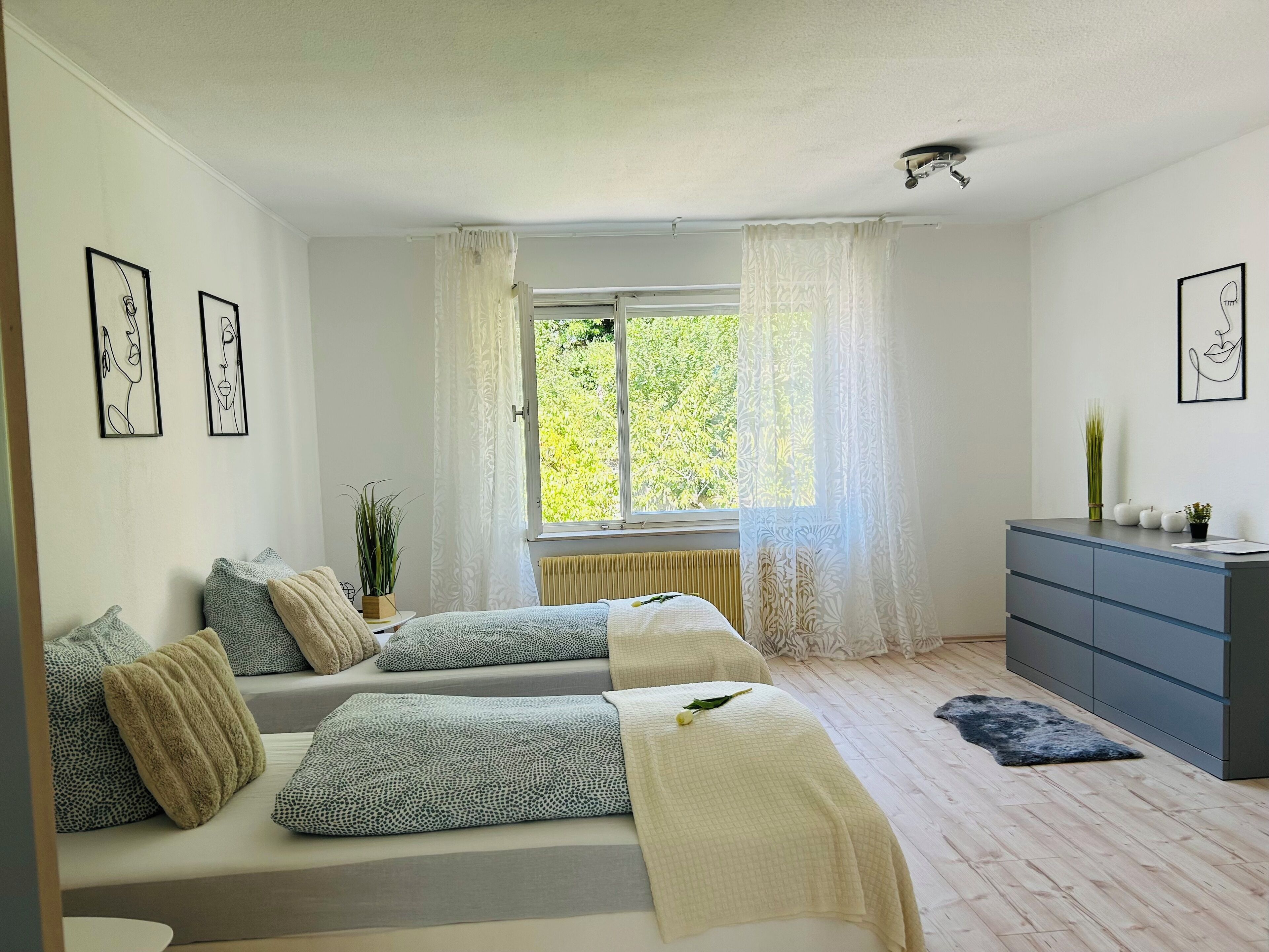 A bedroom with two beds, a dresser, and a window with curtains.