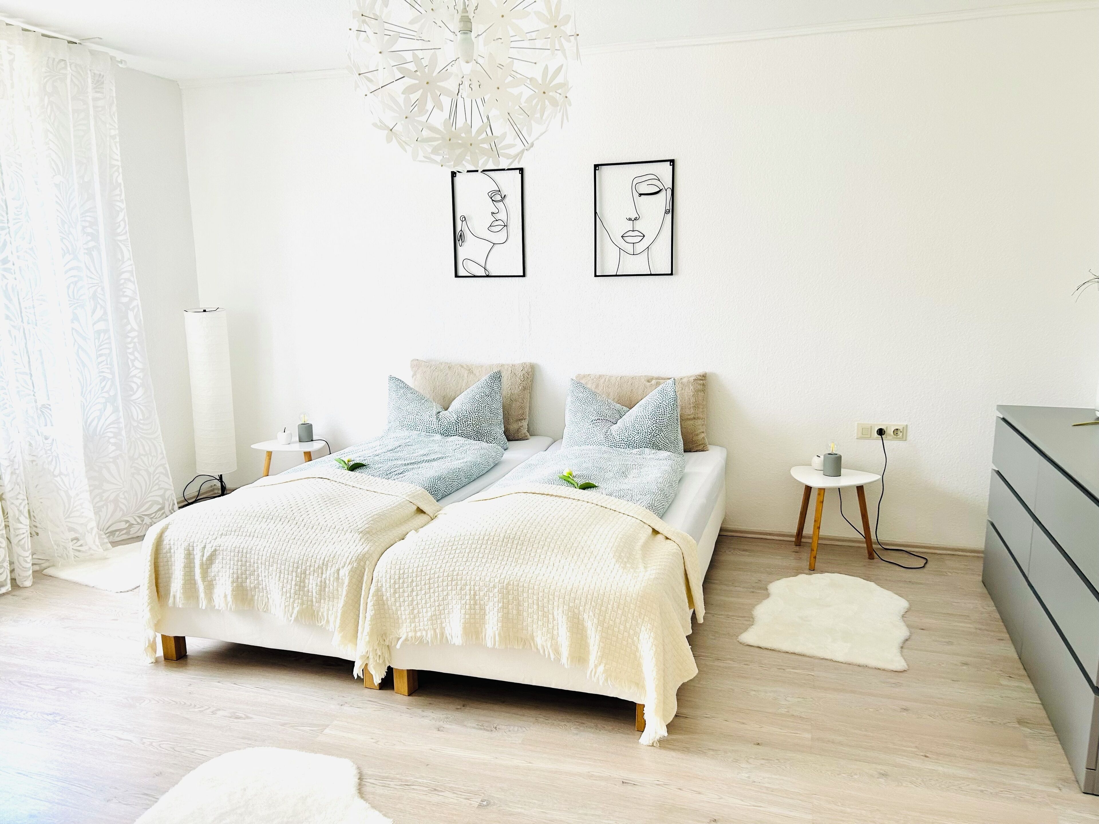 Een moderne slaapkamer met een bed, nachtkastjes, een dressoir en twee kunstwerken aan de muur.
