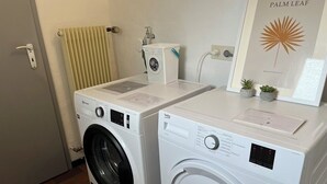 A laundry room with two washing machines, a radiator, a small washing machine, and a framed botanical print on the wall. - Hechingen: AlbGlück 1 Apartment | 2 bedrooms | sleeps 1–5 | 5 km Castle (Hechingen)