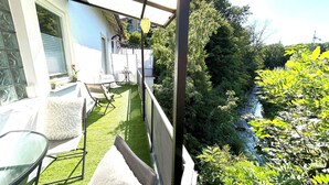 A balcony with a small table and chairs, a white furry rug, and a view of a river and greenery. - Hechingen: AlbGlück 1 Apartment | 2 bedrooms | sleeps 1–5 | 5 km Castle (Hechingen)