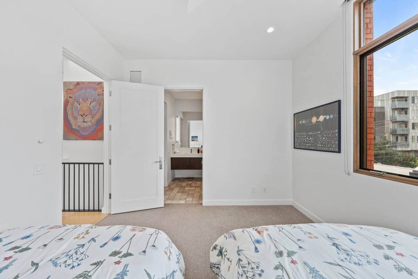A bedroom with two beds, a window, and a door leading to a bathroom.