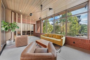 Un interior moderno con sofá, sillón y ventanas amplias que ofrecen vistas a árboles y edificios.