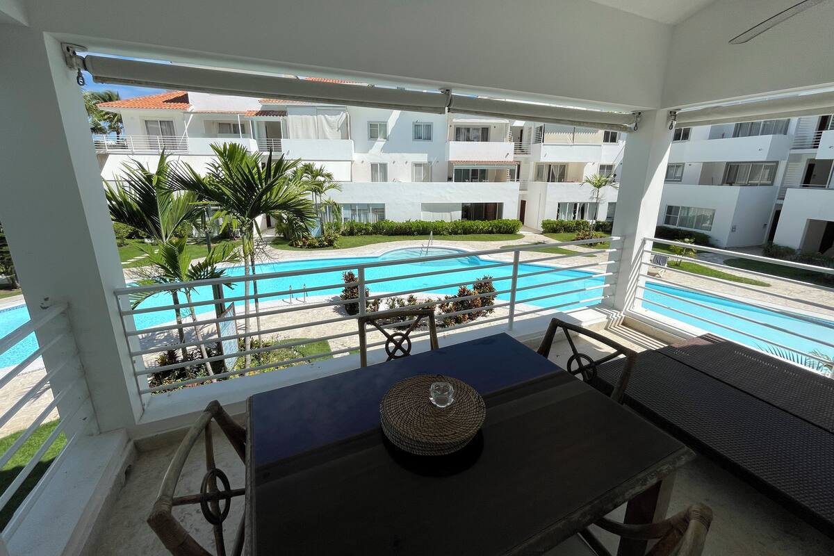 A balcony with a view of a swimming pool, white buildings, and greenery.