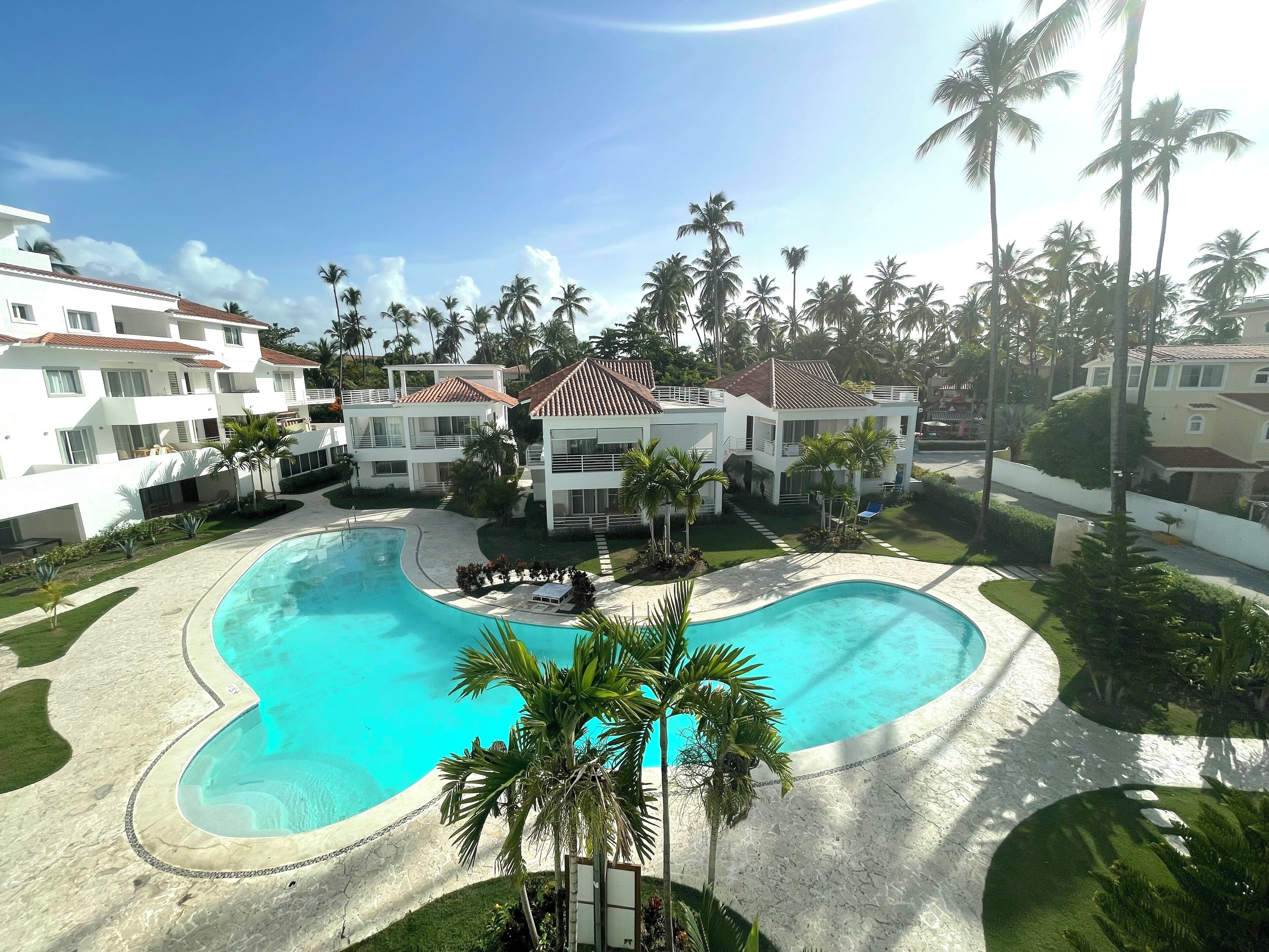 A resort with a large swimming pool, multiple buildings with balconies, and palm trees.