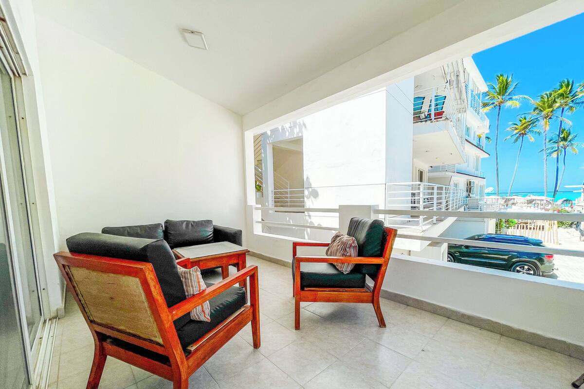 A balcony with a view of the ocean, a wooden chair, a sofa, and a table.