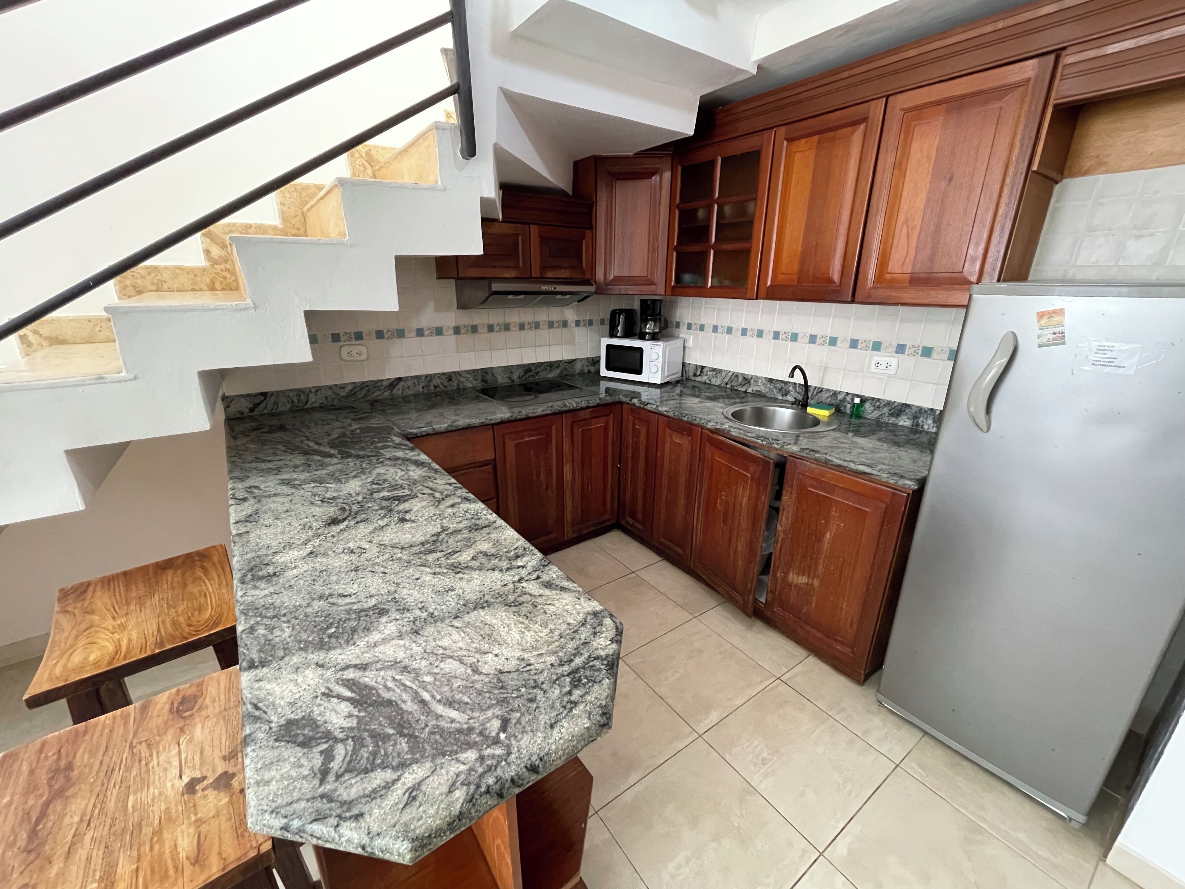 A kitchen with wooden cabinets, a granite countertop, a stainless steel sink, a microwave, and a refrigerator.