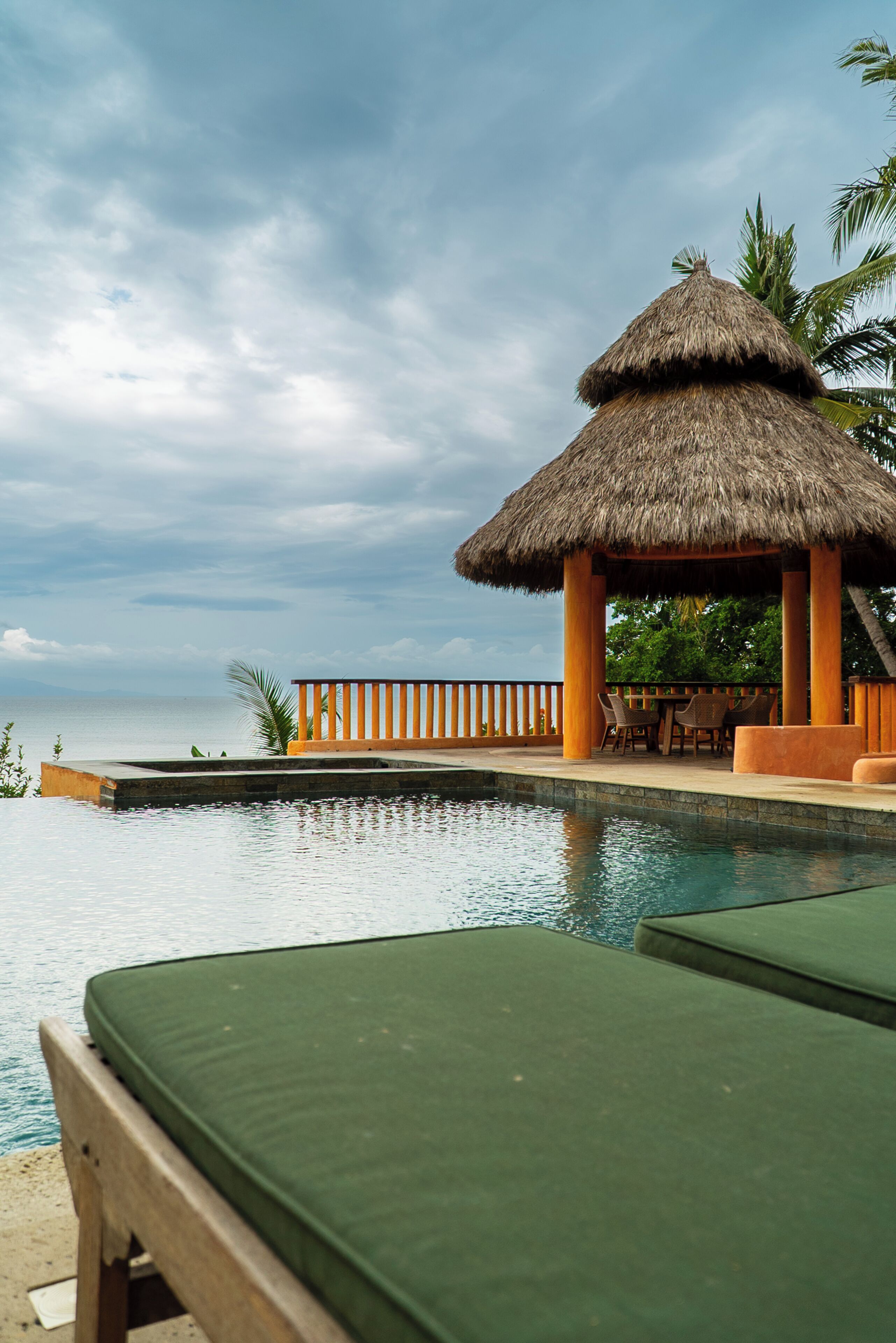 A poolside area with a thatched-roof structure, lounge chairs, and a view of the sea.
