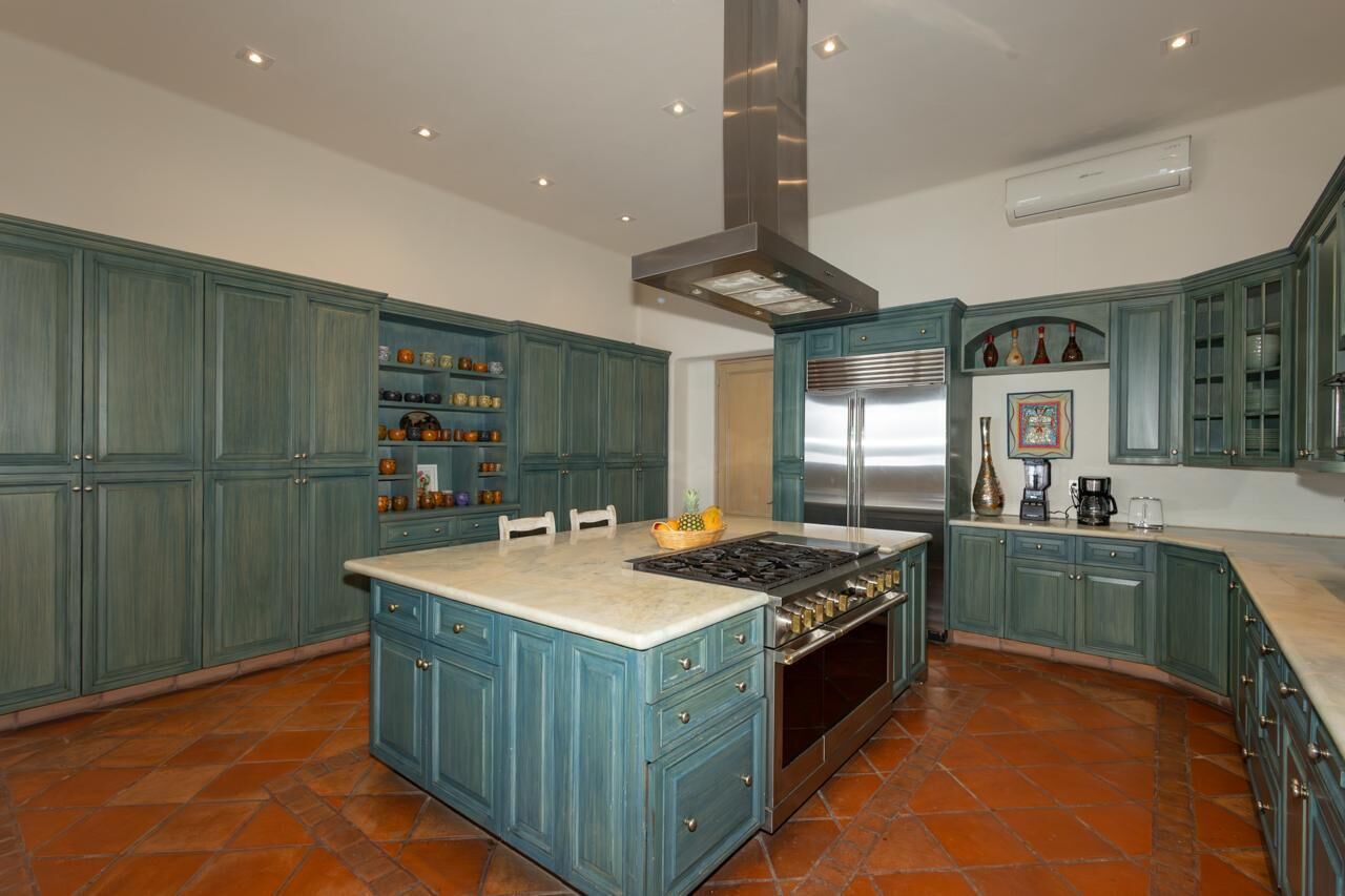 Una cocina con armarios color turquesa, una isla central con estufa y un refrigerador grande.