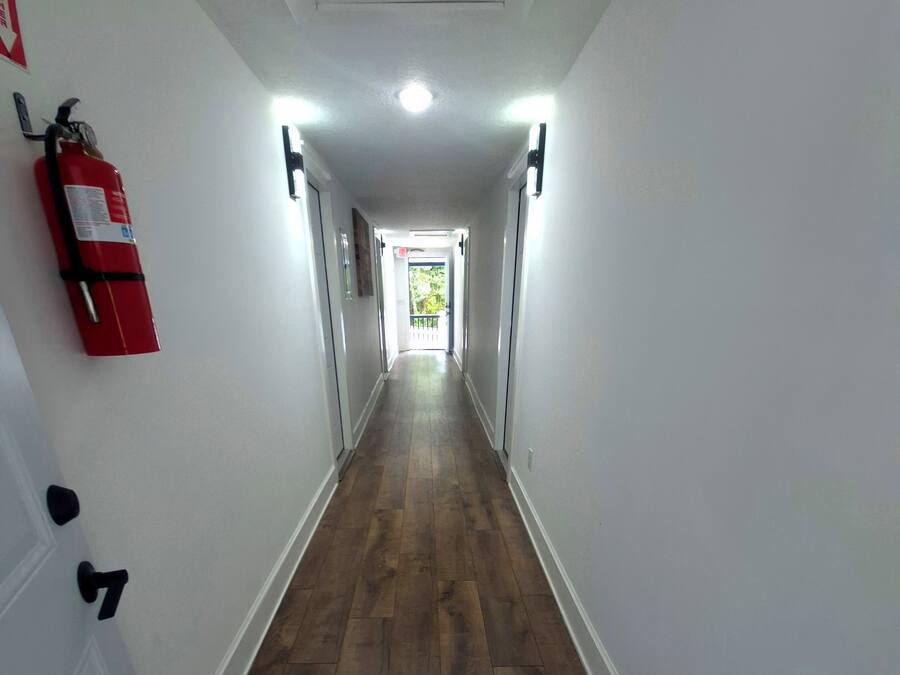 A hallway with wooden flooring, white walls, and a fire extinguisher mounted on the wall.