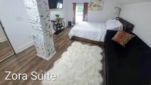 A Zora Suite with a bed, a desk with a plant, a white furry rug, and a painting on the wall. - Zora's Sojourn (St. Augustine)