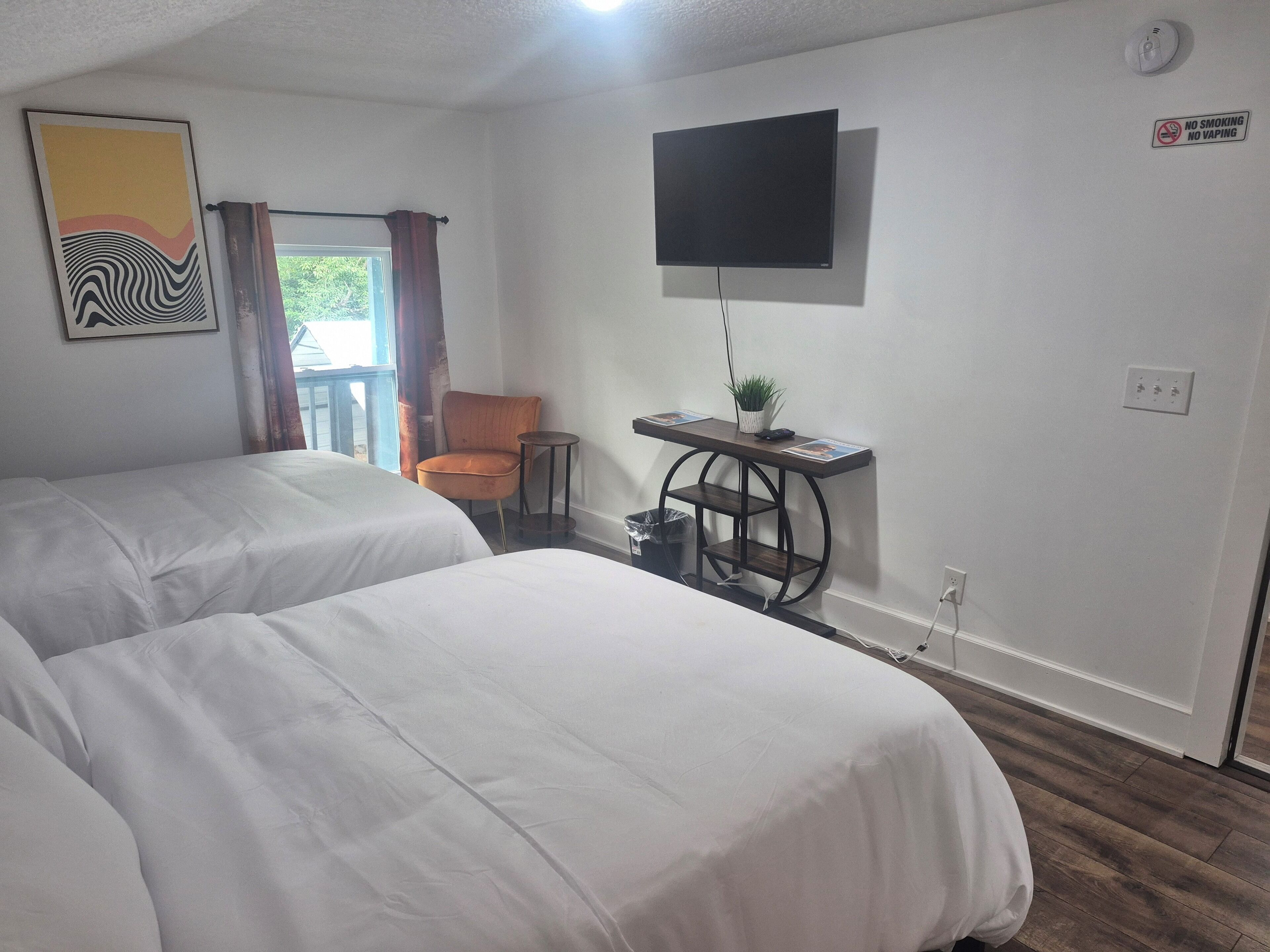 A hotel room with two beds, a desk with a plant, a TV, and a "No Smoking" sign.