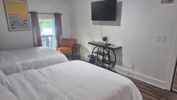 A hotel room with two beds, a desk with a plant, a TV, and a "No Smoking" sign.