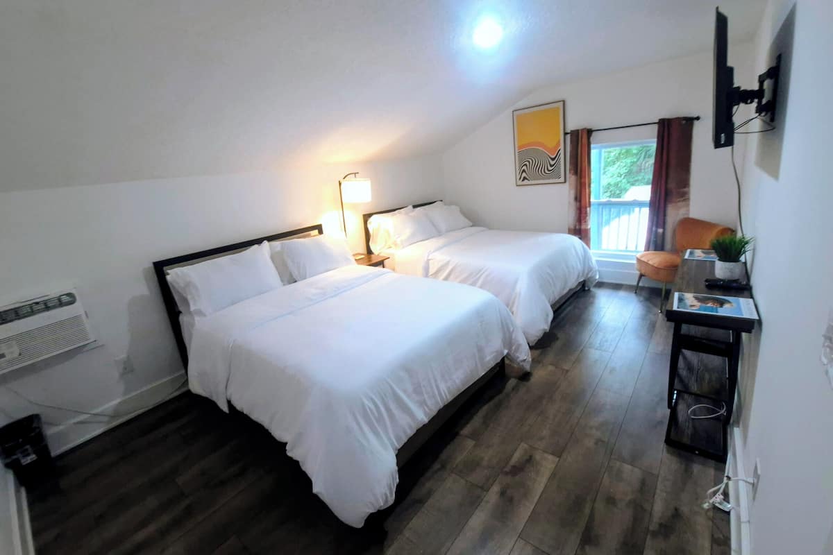 Une chambre d’hôtel avec deux lits, un bureau avec une chaise, une fenêtre avec des rideaux et un téléviseur fixé au mur.