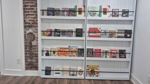 A bookshelf with various books, a brick wall, and a door. - Zora's Sojourn (St. Augustine)