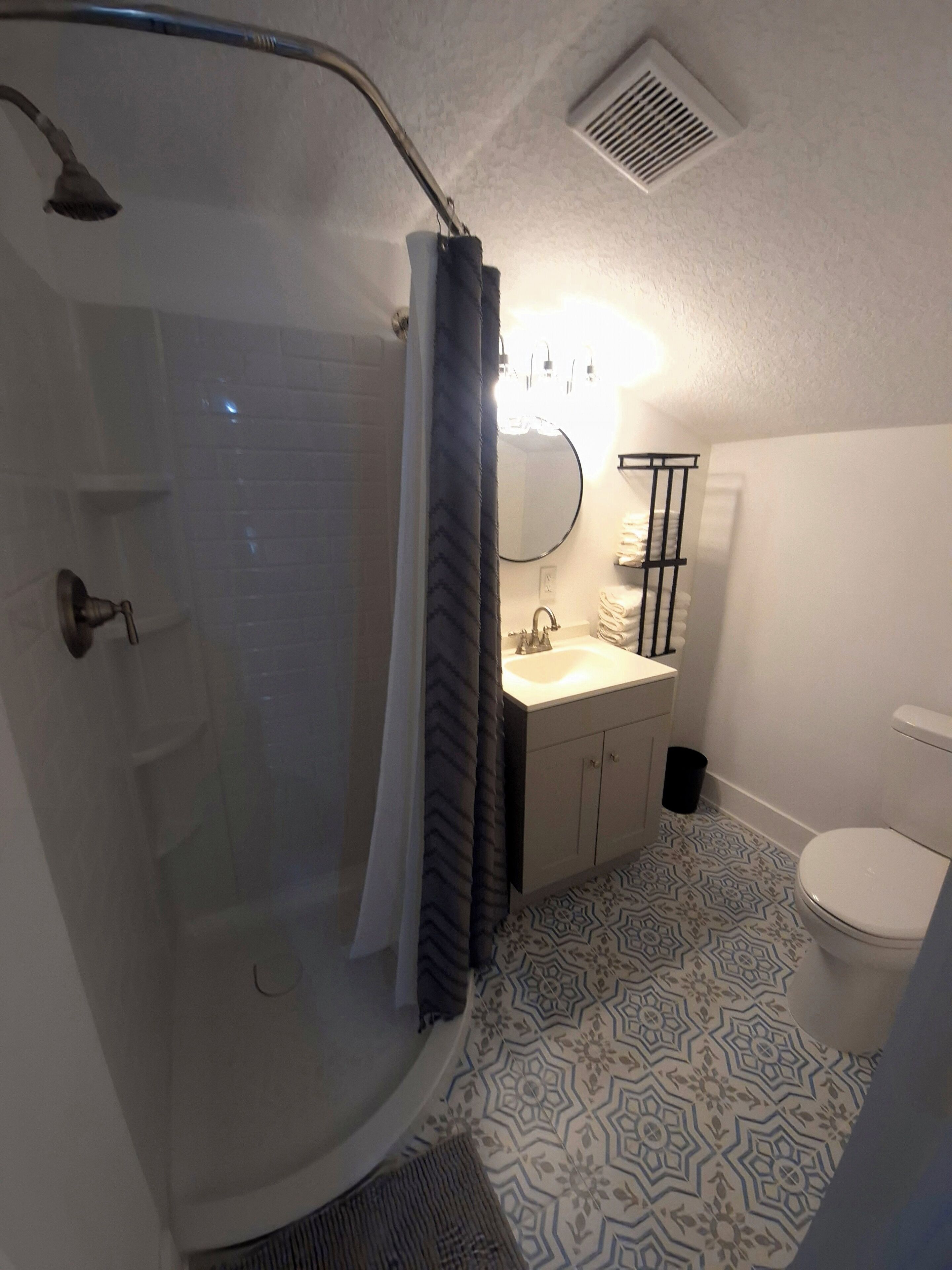 A bathroom with a shower, toilet, sink, and a towel rack.