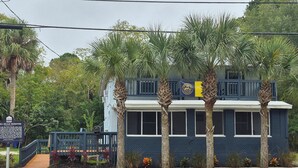 A two-story building with a dark blue exterior and a white trim, featuring a large window and a flag. - Zora's Sojourn (St. Augustine)