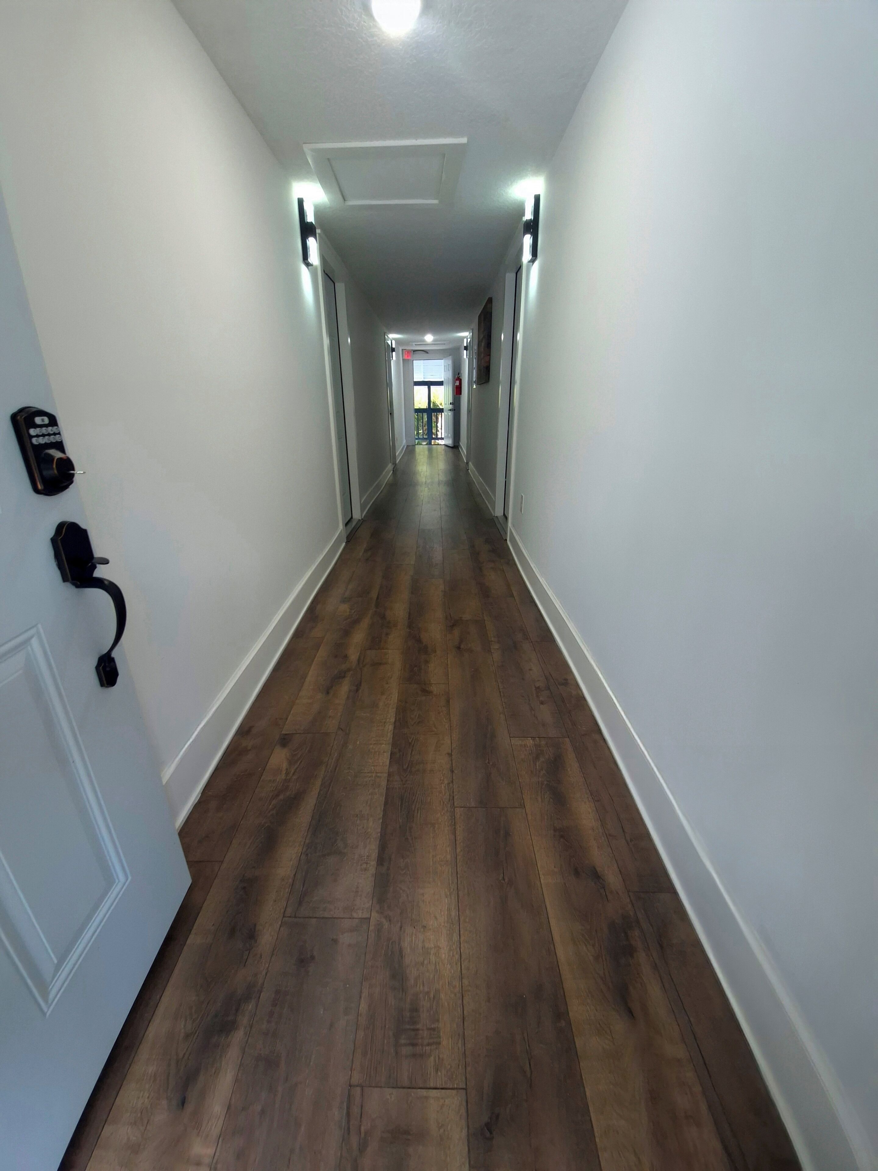 A long, narrow hallway with wooden flooring and white walls.