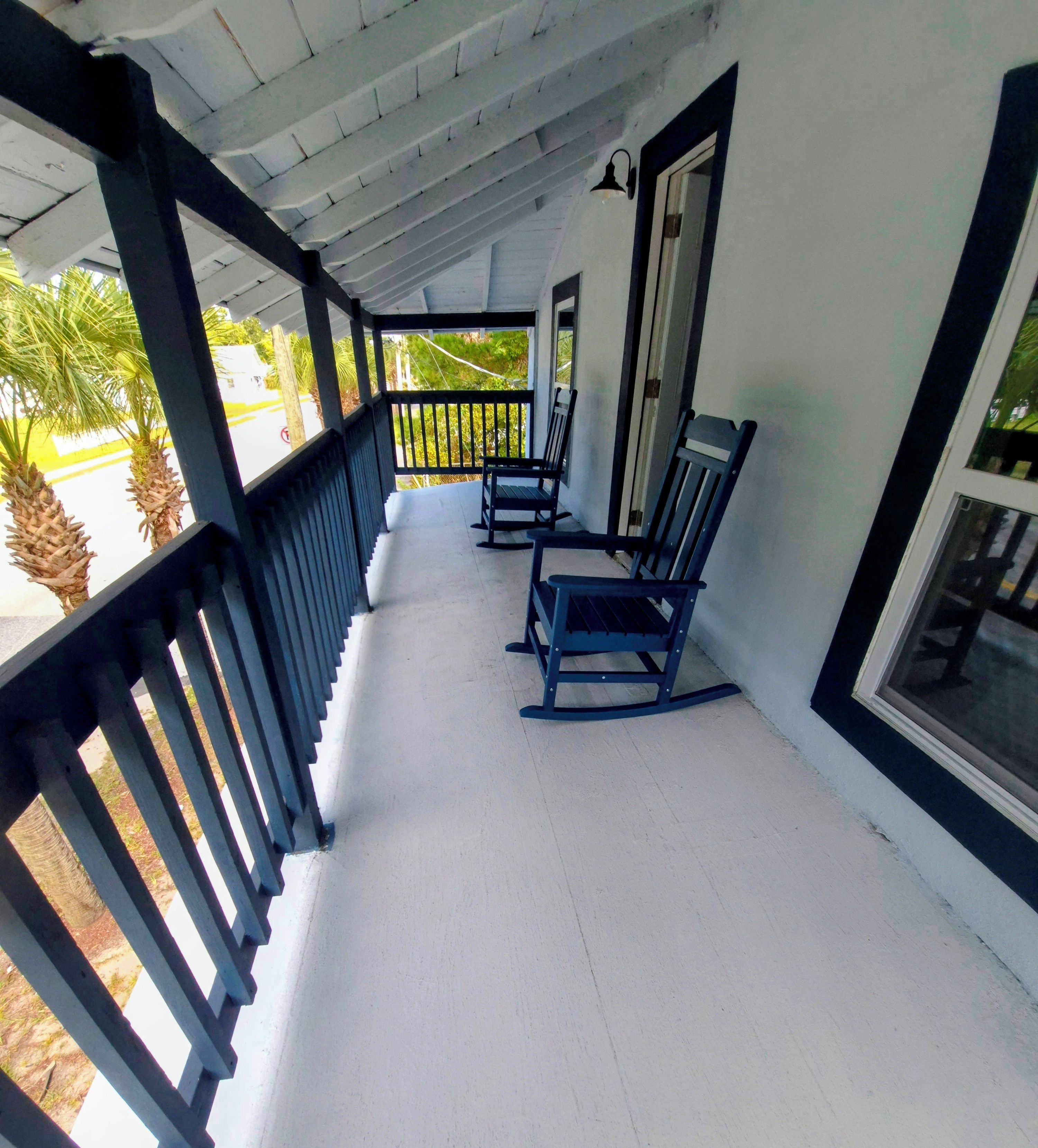 An upper front porch with a white floor, black railings, and two rocking chairs.