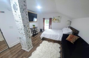 A Zora Suite with a bed, a desk with a plant, a white furry rug, and a painting on the wall. - Zora's Sojourn (St. Augustine)