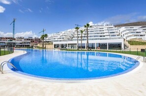 A swimming pool with a clear blue water surface, surrounded by a white building with balconies and palm trees. - La Petite For t Seaview Flat in Marbella (Finestrat)