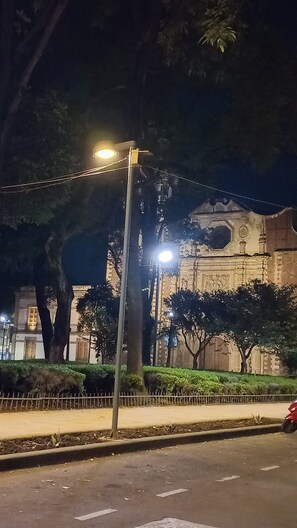Eine beleuchtete Straße bei Nacht mit Straßenlaterne, Bäumen und einem Gebäude mit einem großen Bogenfenster.