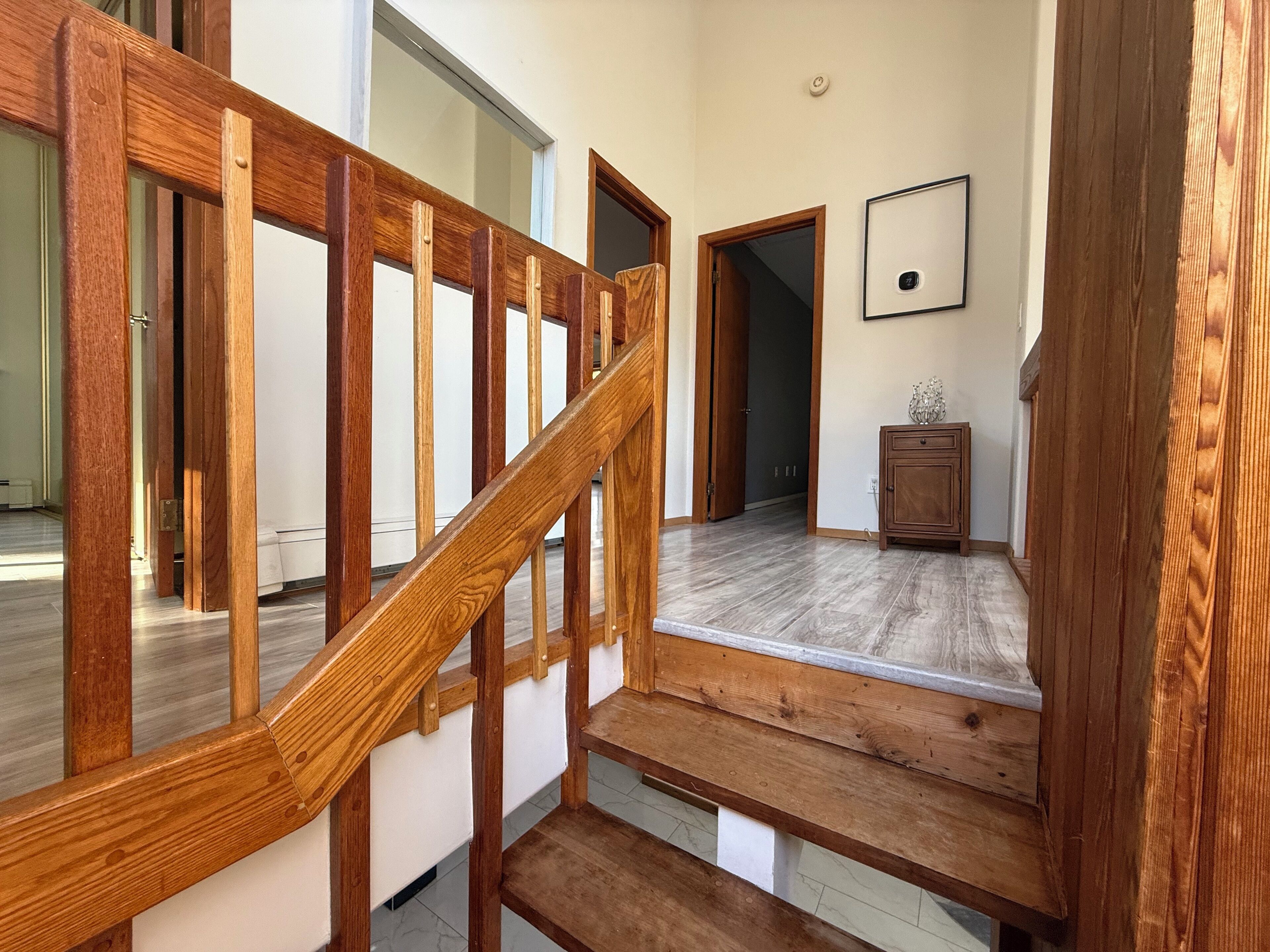 Un escalier en bois menant à un palier avec un mur blanc et un tableau encadré.