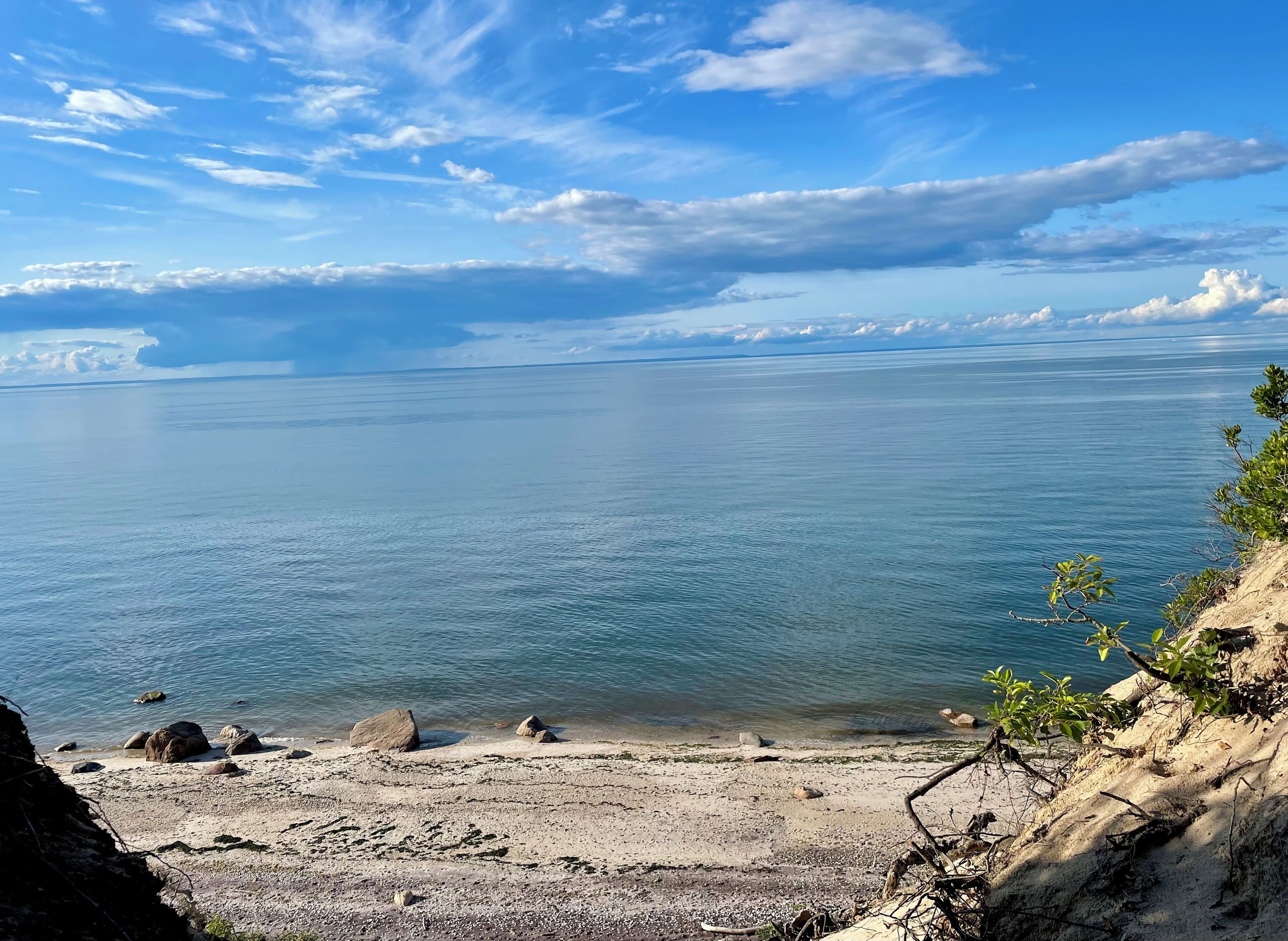 A coastal landscape with a sandy beach, rocky outcrops, and a clear view of the sea under a partly cloudy sky.