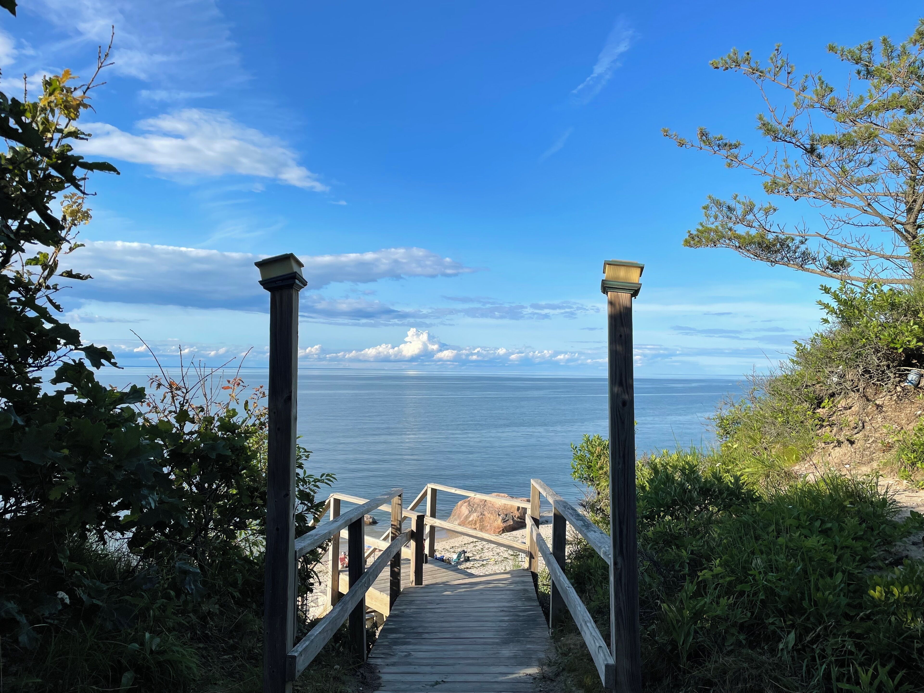 Una escalera de madera que baja a una playa, con vista despejada al océano y montañas a lo lejos.
