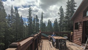 Puinen terassi, jossa on kaide, pöytä ja tuoleja, ja jolta avautuu näkymä metsäiselle alueelle.