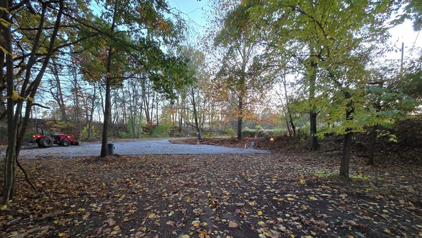 A parking area with a red vehicle, surrounded by trees and covered with fallen leaves. - 50/30 amp all weather campground site #2 full hook up (Masury)