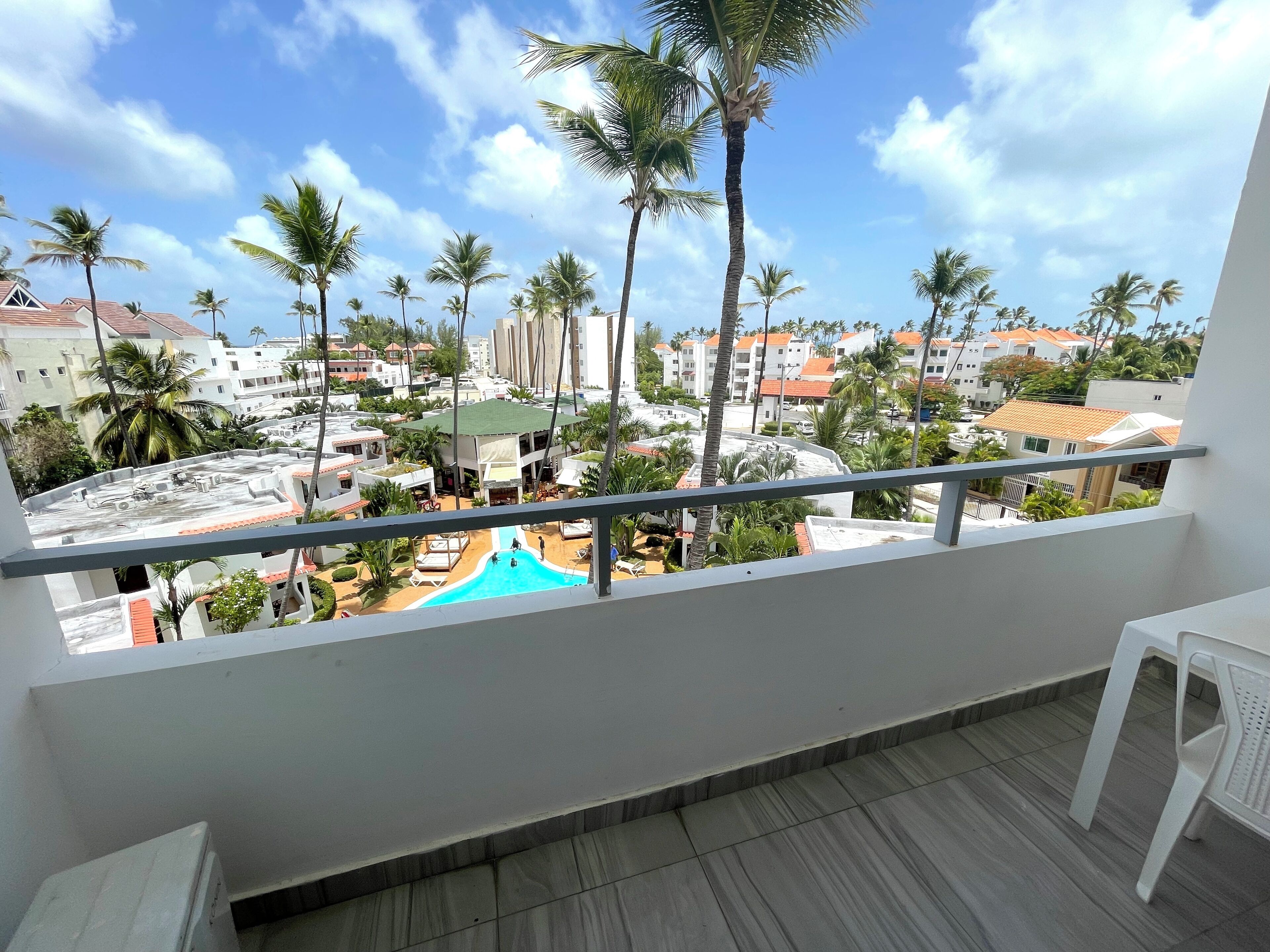 Un balcon offrant une vue sur une piscine, des palmiers et les bâtiments environnants.